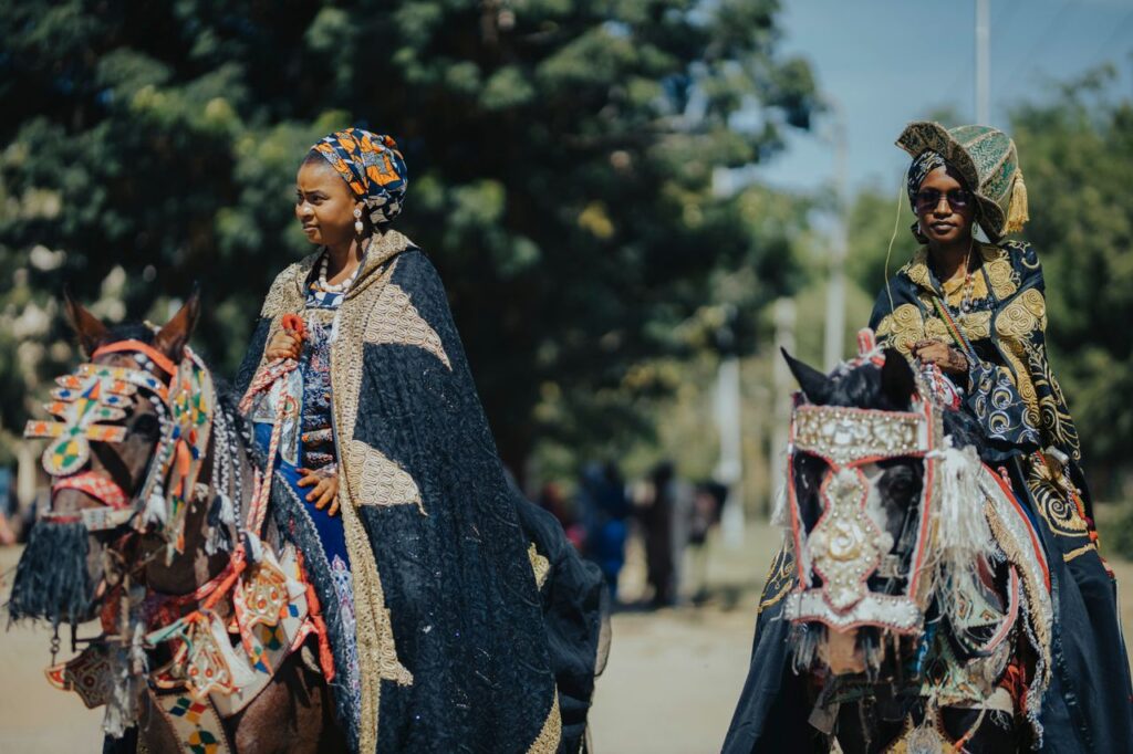 Women in vibrant traditional attire riding decorated horses in an African ceremony.