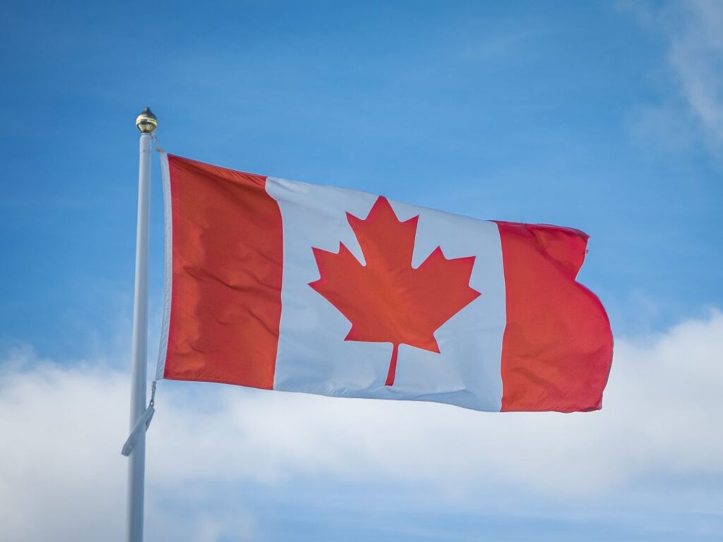 A vibrant Canadian flag waving in the breeze against a bright blue sky, symbolizing national pride.